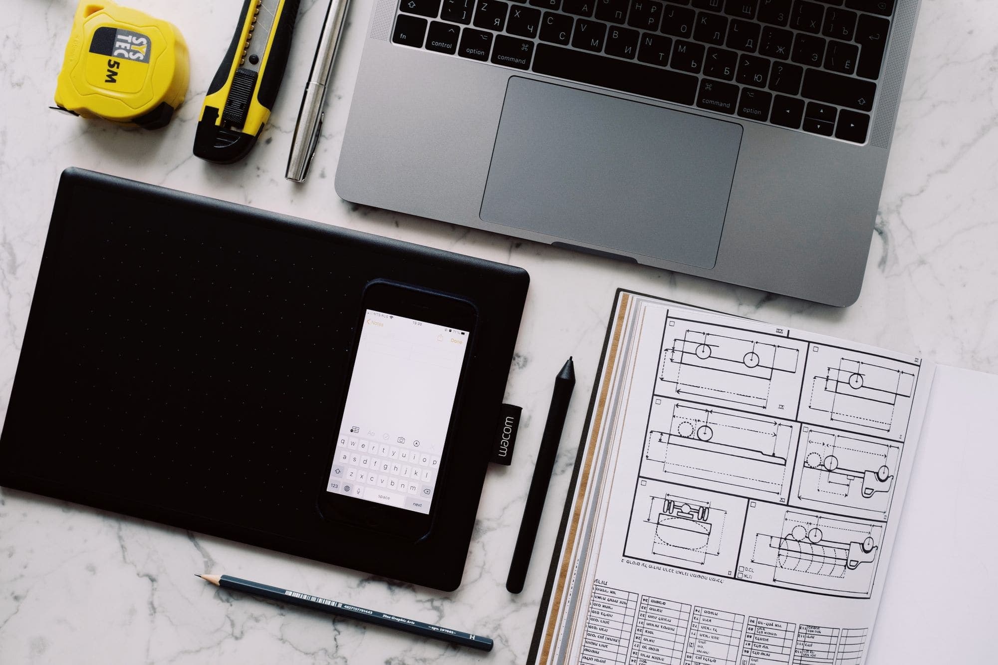 Printed wireframes, a sketchbook and a laptop arranged on a white desk